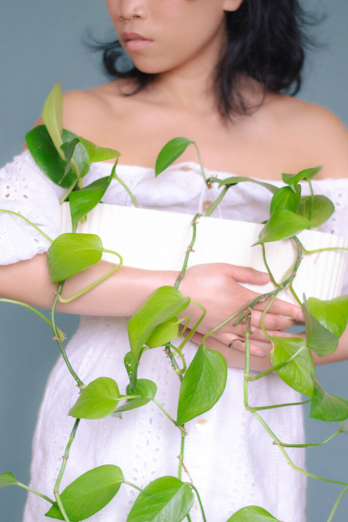 Woman in white eyelet dress holding a green pothos plant to show ethical and sustainable fashion